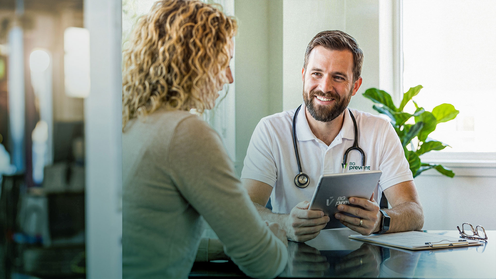 Arzt von BG prevent im Gespräch mit einer Patientin, hält ein Tablet in der Hand.